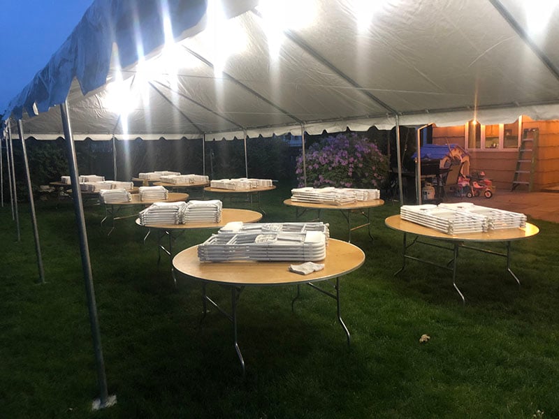 Round tables and folding chairs beneath a party tent with lights